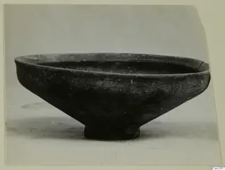 Shallow bowl with a flared rim and short ring foot, dark surface, photographed from the side