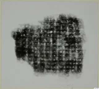 Blurred photograph of a dark, irregular metal mass with a grid-like pattern, possibly iron weapon fragments