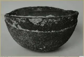 Large heavily corroded metal bowl with encrusted white deposits, photographed on a plain grey background.