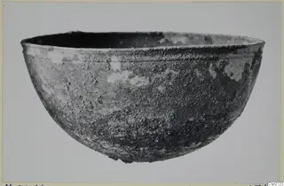 Rounded bowl with a flared rim and an encrusted, corroded surface, shown in side view on a plain background.