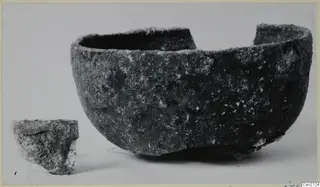 Rounded bowl with a broken rim and a small broken fragment beside it, on a pale background