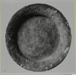 Shallow bowl seen from above, with a broad rim and a rounded central hollow, photographed on a plain grey background.