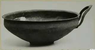Dark grey bowl with a single strap handle and a ring foot, photographed from the side.