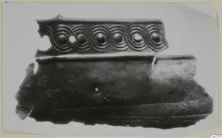 Bronze mounting fragment with a relief band of spiral scrolls enclosing round bosses, on a plain white background.