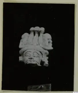 Pale carved head with a tall lobed headdress, photographed against a black background