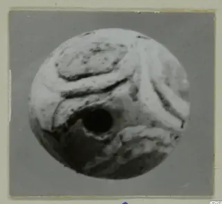 Round bead with a large off-center hole and raised curved ridges across its pale surface
