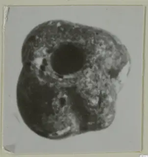 Blurred close-up photograph of a lumpy dark object with a large round hole, from Idalion