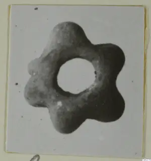 Six-lobed ring-shaped object with a large central hole, grey in colour, shown close up