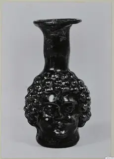 Dark glass flask shaped as a head, with bead-like curls of hair and a tall flared neck
