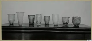 Row of several blown glass vessels standing on a dark wooden surface, Vouni