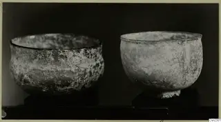 Two blown glass bowls, one wide and one with a footed base, on dark stands against a black background.