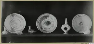 Three shallow dishes and several small vases standing in a row on a shelf against a dark background