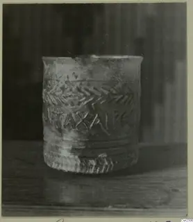 Small straight-sided cup with raised lettering and chevron bands, standing on a wooden surface