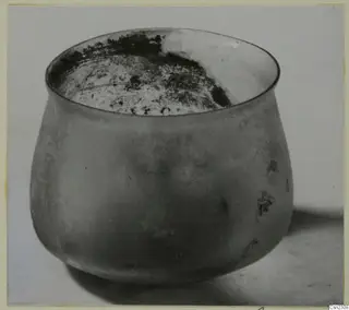 Blown glass jar with a wide, flared rim and weathered surface, shown on a plain surface.