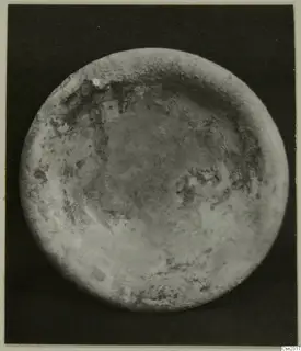 Blown glass object seen from above: a round piece with a raised rim and a weathered, mottled surface