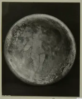 Blown glass object seen from above, with a faint upright pattern across its round surface.