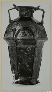 Blown glass vessel with two handles, a faceted body and raised relief decoration, standing on a metal stand