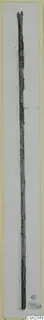 Long, narrow corroded metal object lying lengthwise on a pale card.
