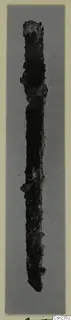 Corroded iron knife, upright against a grey background, shown on a photo mount.