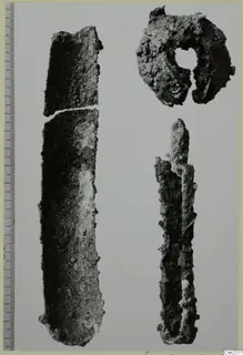 Three corroded iron objects: a long flat blade broken in two, a ring-shaped piece, and a narrow split object, with a scale bar at left.