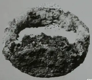 Corroded, encrusted metal object, roughly oval, with a pale hollow across its upper part