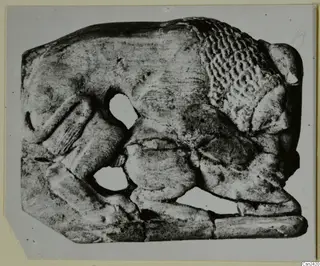 Carved relief plaque with a figure in low relief and irregular openings, photographed on a grey card