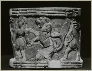 Carved cylindrical bone object with relief of a lion and a standing figure, ridged bands at top and base