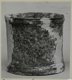 Cylindrical object with an open top and flared base, pale surface partly covered by dark encrusted deposits