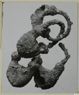 Corroded silver object, a tangle of loops and lumpy forms, shown against a plain pale grey background.
