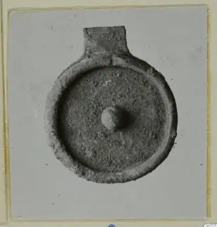 Silver find: a round flat object with a raised rim, a rectangular tab at the top and a small central knob
