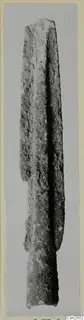 Corroded metal weapon blade with a central ridge, photographed upright against a grey background.