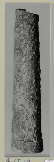Long, tapering bronze object with a corroded surface, probably a weapon fragment, shown upright against a grey background