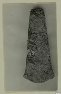 Corroded flat metal blade or axe-head from Lapithos, photographed on grey card.