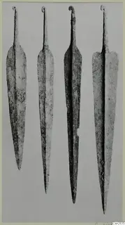 Four long metal weapon blades standing upright side by side, each with a curled tang at the top, on a grey background.