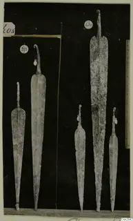 Five metal blades with tangs, photographed against a black background with number labels and a scale ruler.