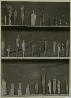 Metal weapons and tools laid out in three rows on wooden shelves against a dark cloth backdrop