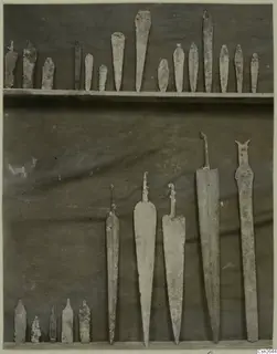 Metal spearheads, daggers and tanged blades laid out in rows against a dark cloth.