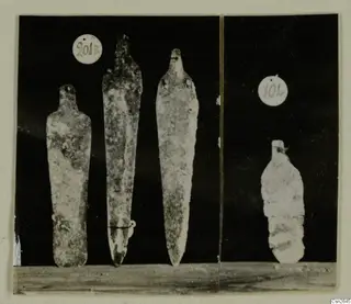 Four corroded metal blades with tangs, shown upright on a wooden surface, in two numbered groups.
