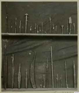 Corroded metal weapons and tools laid out in two rows on a dark cloth