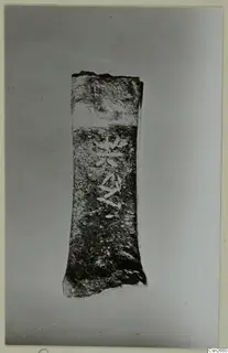 Corroded bronze tool, a flat tapering piece photographed upright on a grey backdrop.