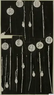 Bronze pins or needles, each tied to a round numbered paper tag, laid out on a dark background