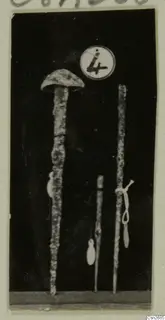 Three metal tools standing upright against a dark background, with a round number label above them