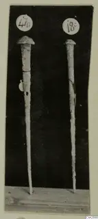 Two long metal tools with domed heads standing upright, each marked with a round number label