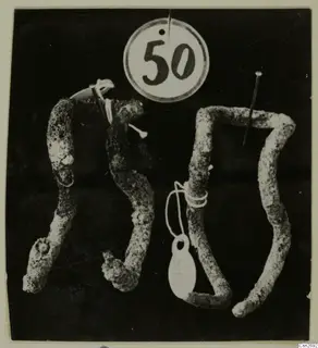 Four corroded bronze tools against a dark background, with a round number label hung above them