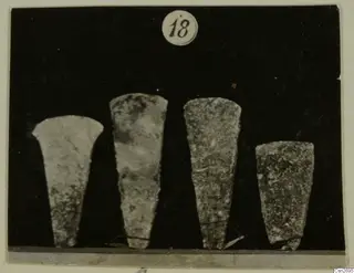 Four flat, tapering bronze tools standing in a row, with a number label above them