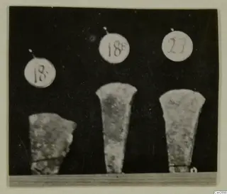 Three bronze tools photographed side by side against a dark background, each with a round number label above it.