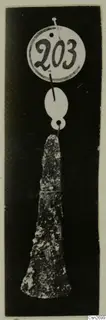 Corroded metal tool hanging from two white tags against a dark background
