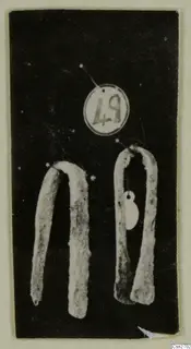 Two bent bronze tools on a dark background, with a round number label above them