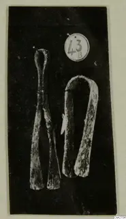 Two corroded bronze tools on a dark background, one a pair of tongs with a looped top and flat ends.