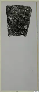 Corroded metal fragment, probably part of a bronze tool, shown on a grey card.
